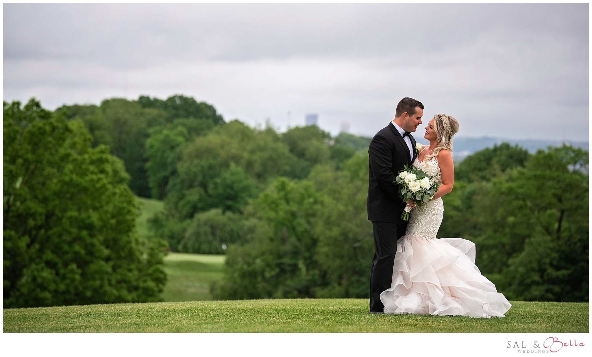 Bride and groom pose for a photo on the hill at Shannopin Country club. Beautiful treeline and pittsburgh in the background.