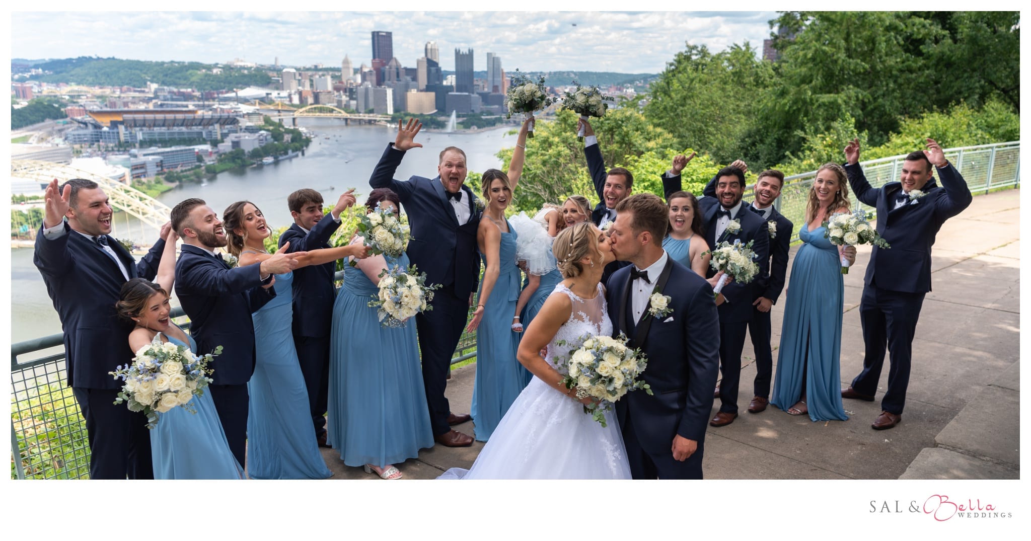 bridal party share in a fun pose with pittsburgh city skyline in the background
