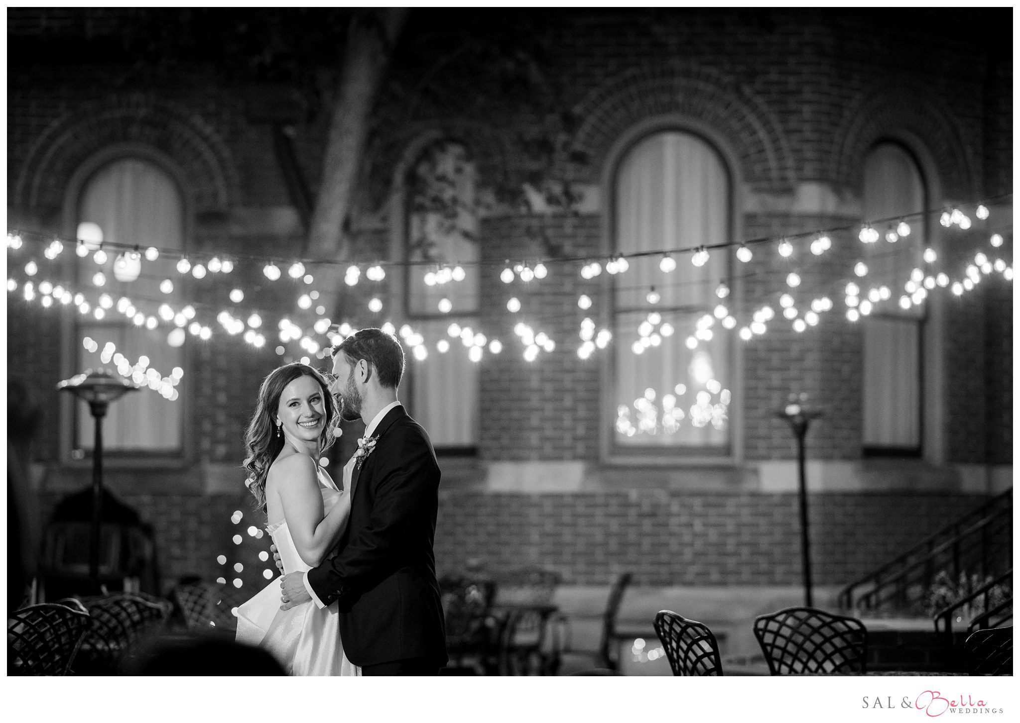 bride and groom pose infront of the twinkle lights in the courtyard of the grand hall at the priory. 