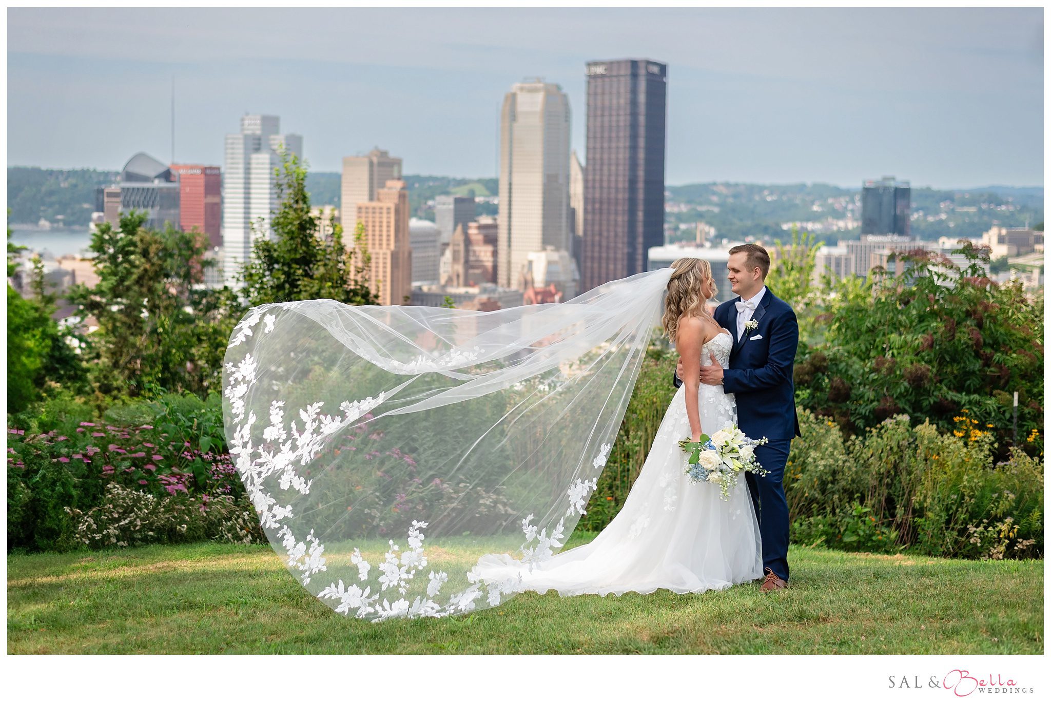 Bride's veil blows in the wind as the pose for wedding photos. The Pittsburgh skyline in the background. 