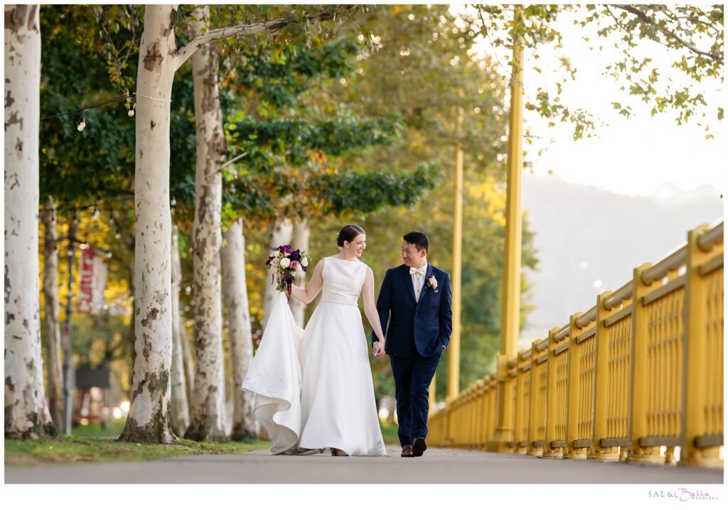 Newlywed couple walks hand in hand near the Roberto Clemente Bridge & the Renaissance. 