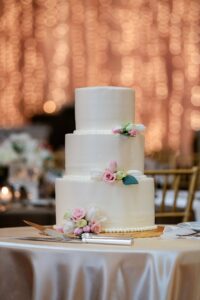 A simple 3-tier wedding cake with the twinkling lights of the Priory grand hall behind it.
