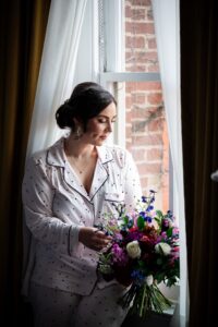 bride sits in the window of the Priory Hotel and looks through her beautiful fall wedding bouquet.