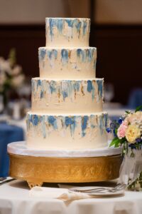 a gorgeous 4-tier wedding cake on a gold stand with blue accents at the Priory