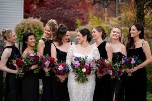 bridesmaids in black pose with the bride in the priory garden, holding beautiful fall-inspired bouquets.