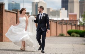 A couple walks together near the priory with pittsburgh skyline in the background.