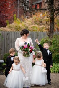 A bride poses with her flower girls and ring bearers in the priory garden.