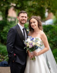 Bride & Groom poses for a photo together in the priory garden. The bride is holding a pretty spring bouquet with hints of blue and purple.
