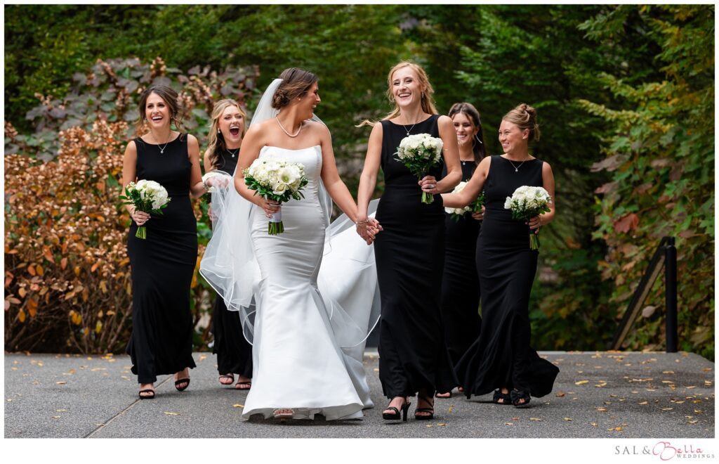 Bride walking and laughing with her bridesmaids in black dresses at Mellon Green in Pittsburgh