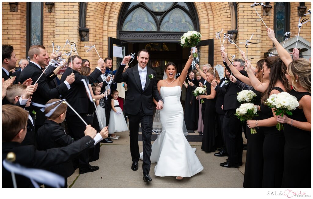 Newlyweds Elle and Mike celebrate outside St. Mary of the Mount as their wedding party waves ribbon wands